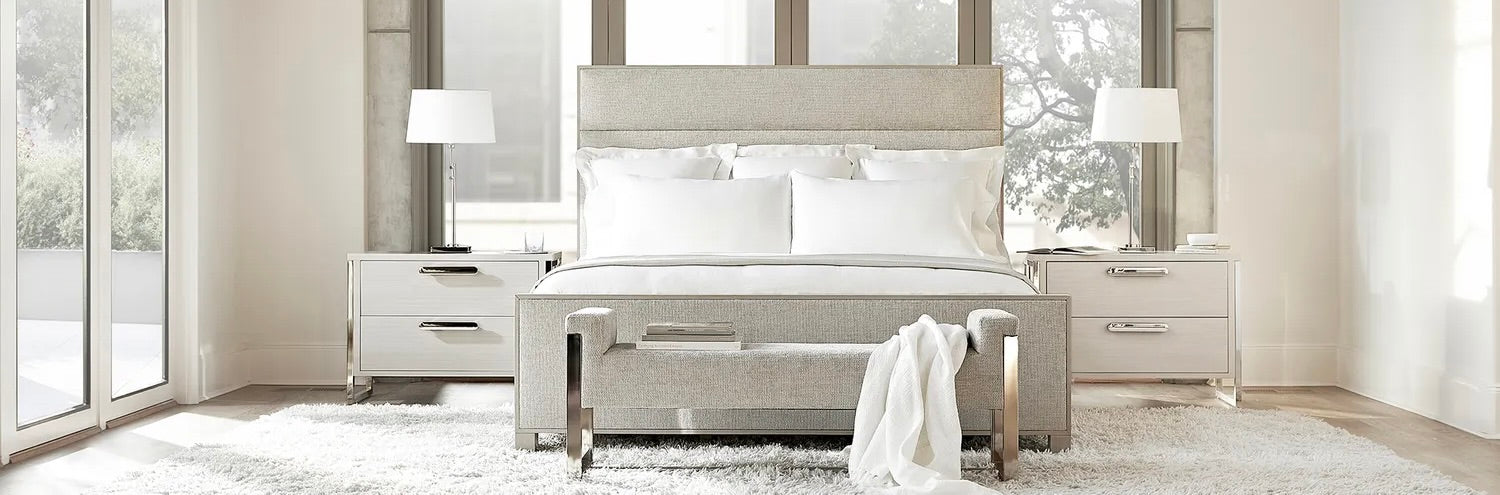 Modern bedroom with upholstered king bed, matching bench, and mirrored nightstands with white lamps, styled in a neutral palette with floor-to-ceiling windows