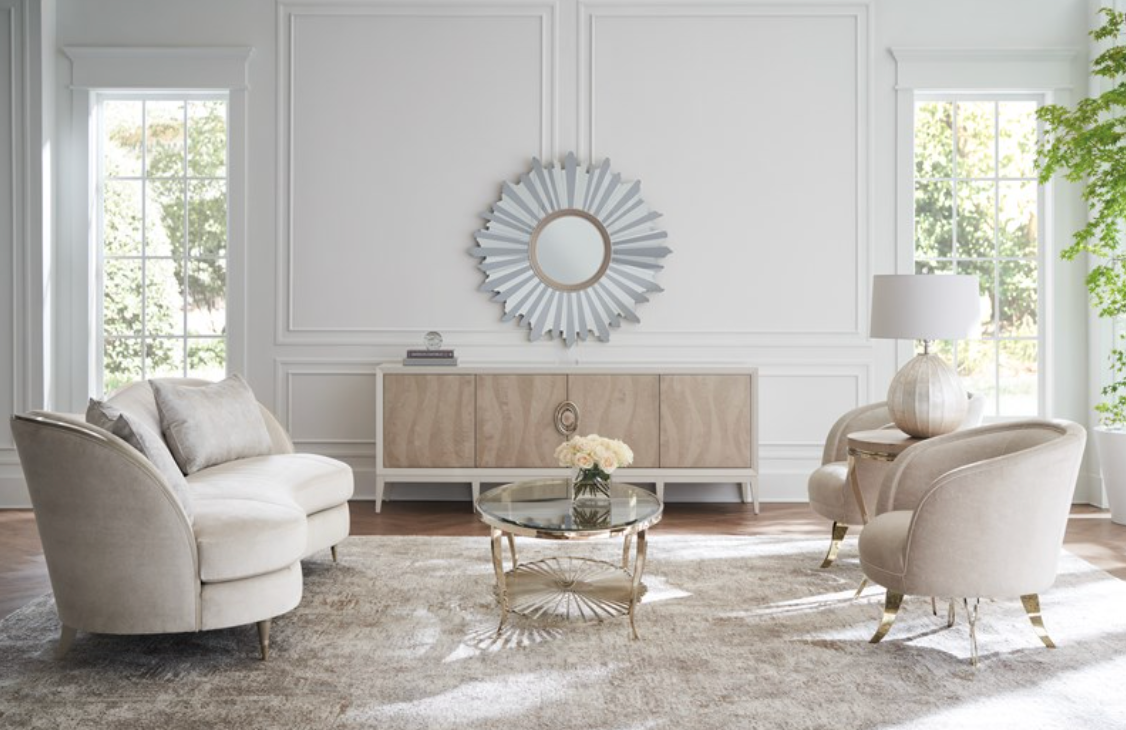 Neutral-toned luxury living room with light wood cabinet, sunburst mirror, round glass coffee table, and velvet seating on a textured rug