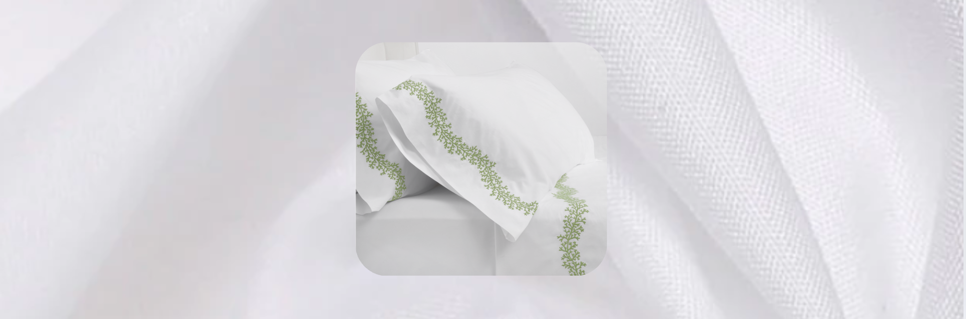 White bed sheets with green embroidered vine detailing on pillowcases, styled against a soft white textured fabric background