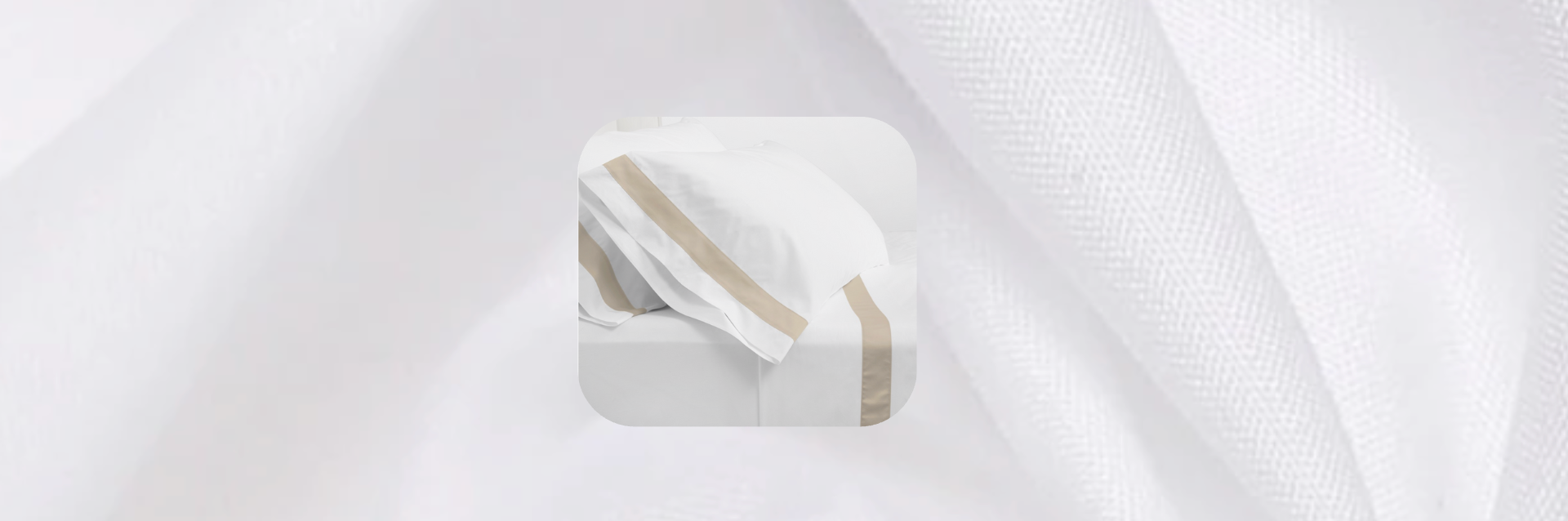 White bed sheets with taupe embroidered border detail on pillowcases, displayed on a bed with a soft white textured fabric background