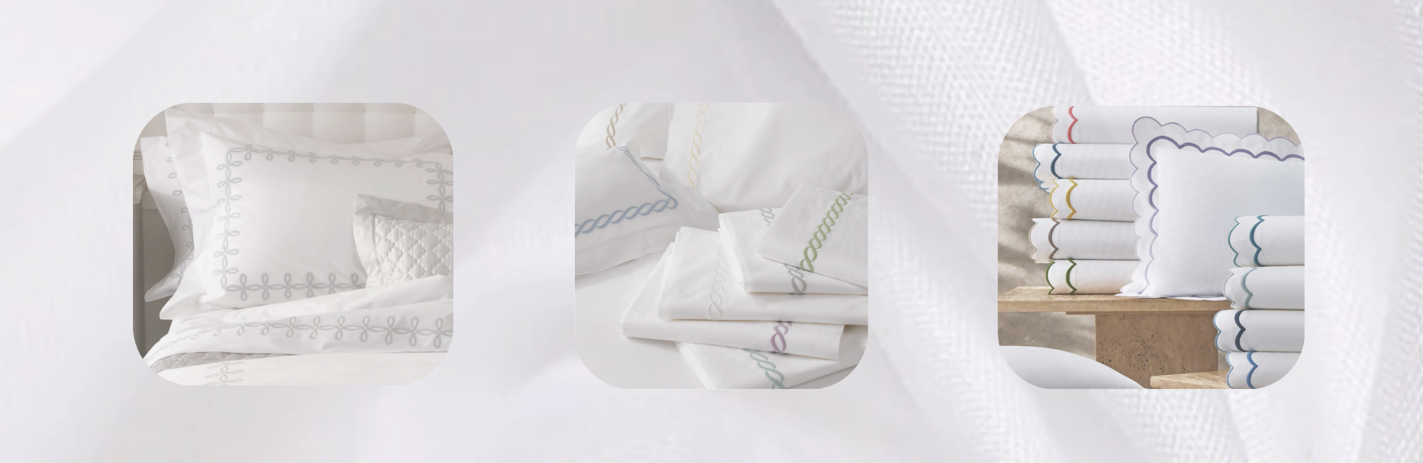 White bed sheets featuring colorful embroidered borders in scalloped, chain, and geometric patterns, neatly folded and stacked on a soft white background