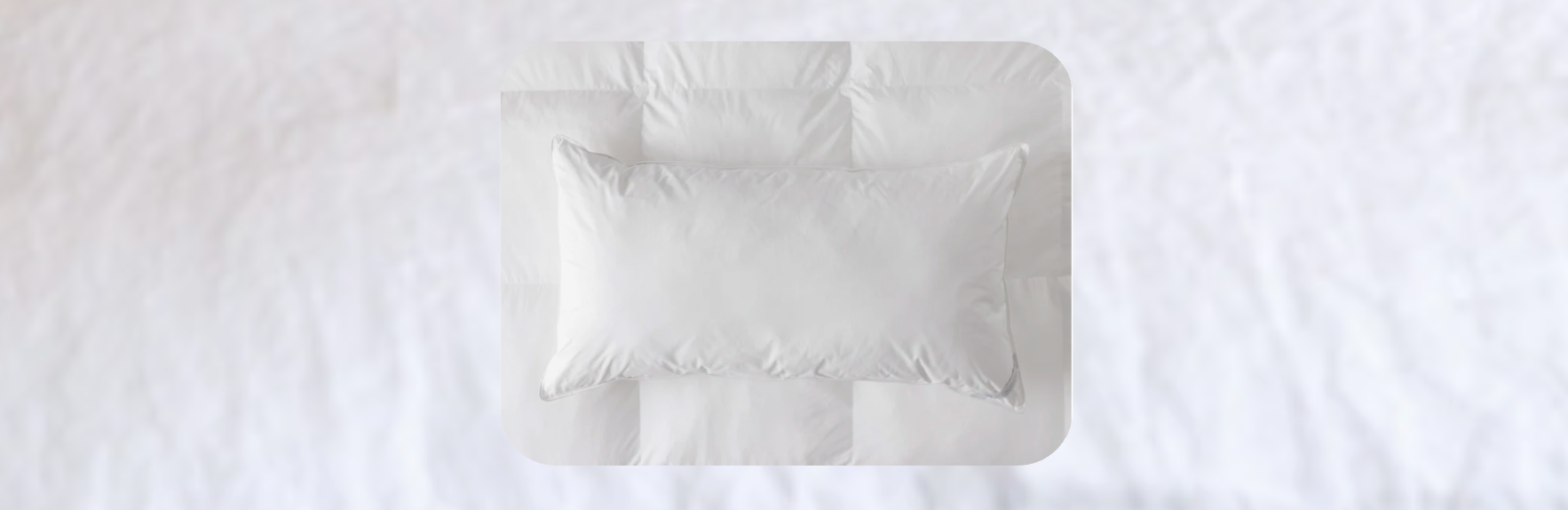 White down or down-alternative pillow placed on a neatly made white bed, styled with subtle stitched detailing in a soft, minimalist bedroom setting