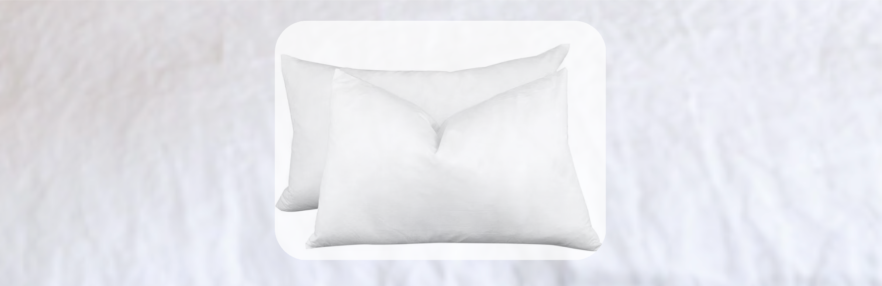 Pair of white bed pillows with smooth fabric finish, layered neatly on a soft white bedspread in a minimalist bedroom setting