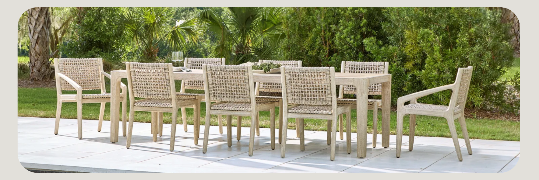 Outdoor dining setup featuring a long rectangular table surrounded by ten light wood woven-back chairs. 