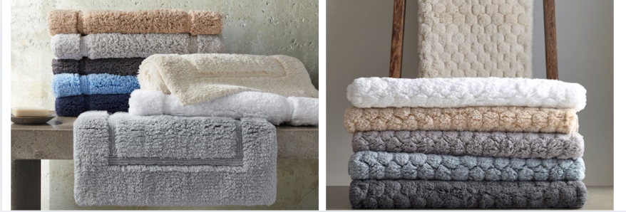 Neatly stacked luxury bath towels in a palette of soft neutrals, blues, and charcoal tones. Featuring textured patterns and plush finishes, styled on wooden benches and ladders for a cozy, spa-like display.