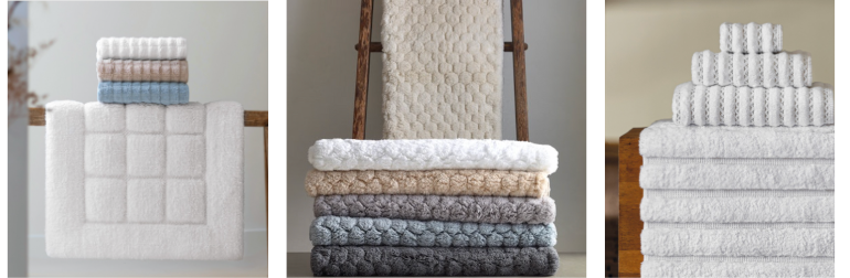 Stacked and folded luxury bath towels in soft, neutral tones including white, sand, grey, and blue. Displayed with textured patterns and elegant finishes, showcasing plush, high-end cotton perfect for spa-inspired bathroom styling.